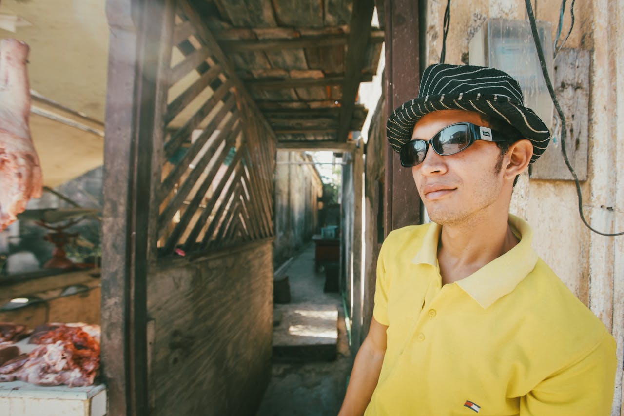 services-03 Casual man in yellow polo shirt with sunglasses and hat standing in a rustic urban area.